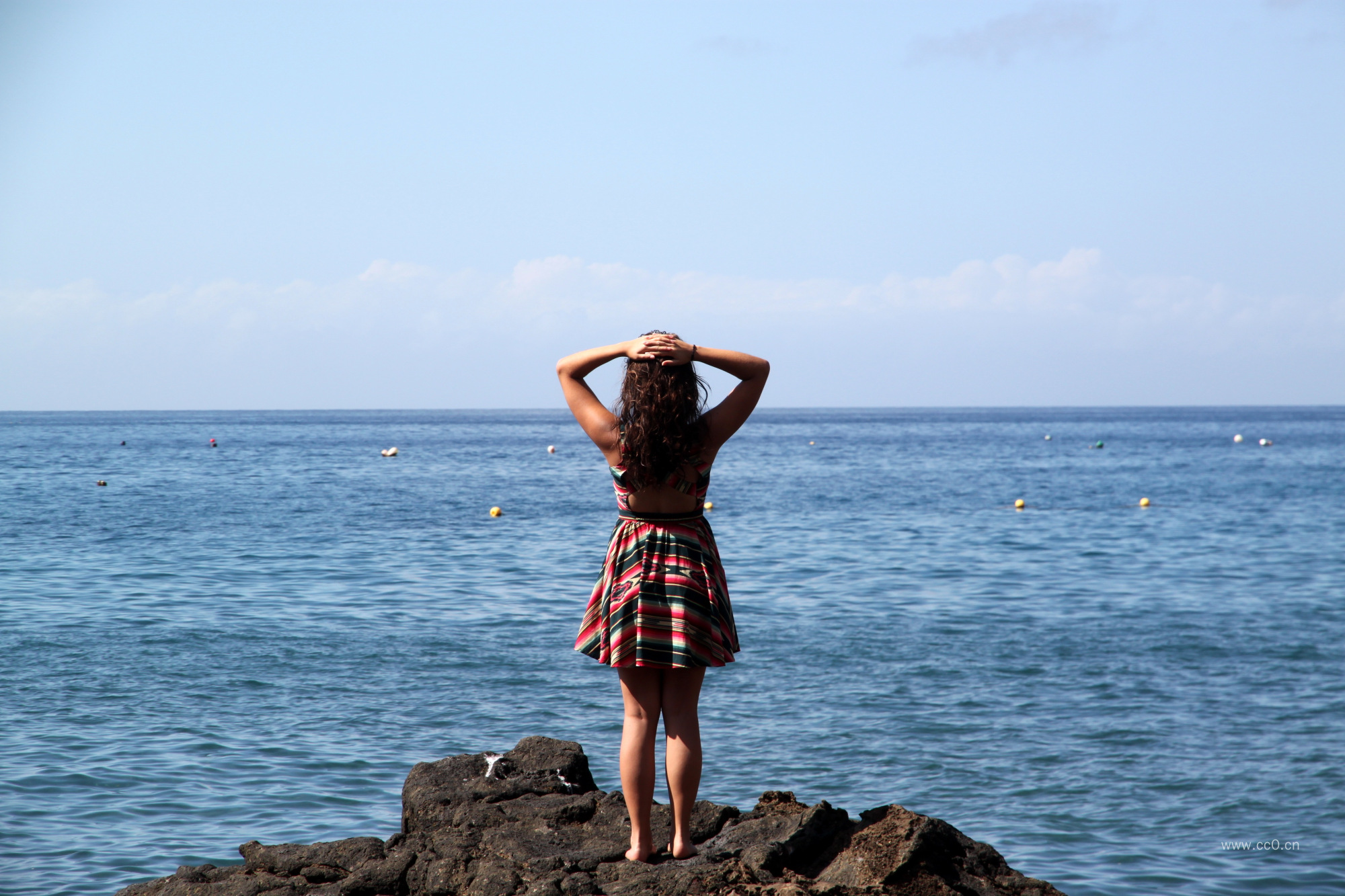 穿着连衣裙站在海边岩石上的女生人物背影
