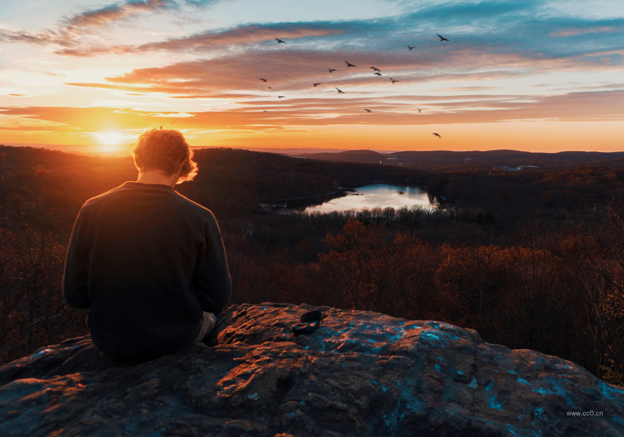 夕阳时分坐在岩石上的男生背影